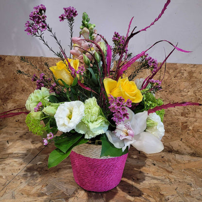 The Flower Arrangement by ReCreation Flowers features yellow roses, white lilies, spring blooms, and light green carnations in a pink basket—beautifully hand-delivered for any occasion.