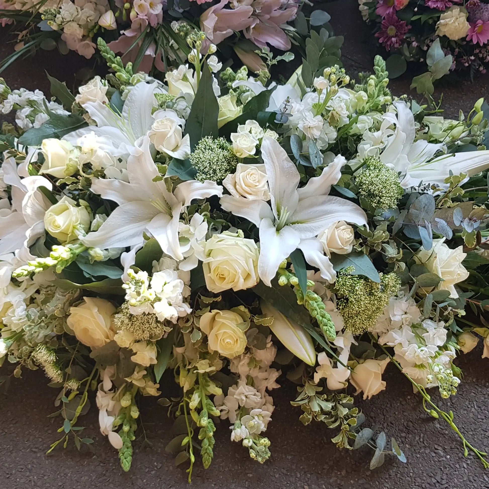 The Casket Spray Funeral Flowers by ReCreation Flowers features white lilies, roses, and lush greenery—an elegant tribute to honor your loved one with beautiful funeral flowers.