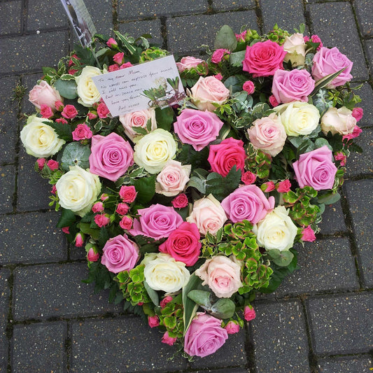 The Solid Heart Funeral Flowers - Loose Style by ReCreation Flowers features pink, white, and cream roses with greenery and seasonal blooms. A handwritten note is included, making a heartfelt tribute for any funeral.