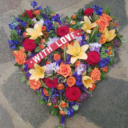 The Solid Heart Funeral Flowers - Loose Style by ReCreation Flowers features seasonal blooms in vibrant hues with a "WITH LOVE" ribbon, arranged on stone—an ideal heartfelt tribute for funerals.