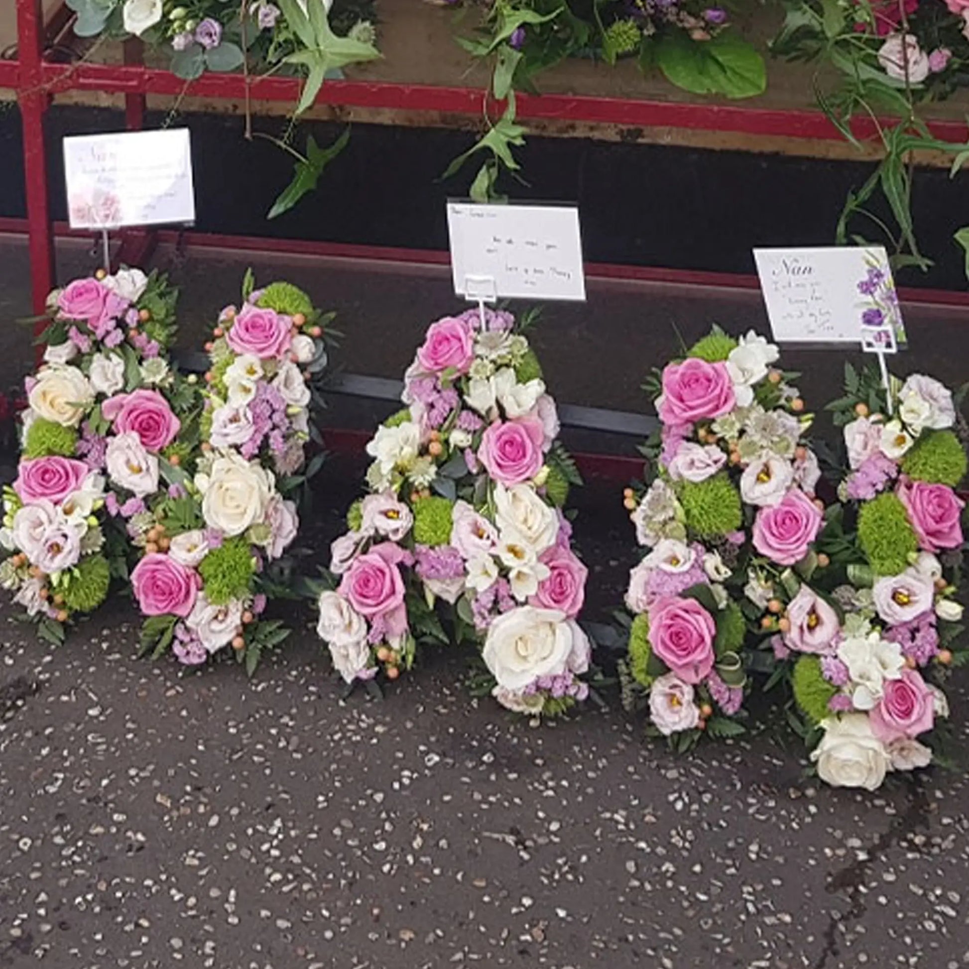 Funeral Flower Letters – Open Loose Style by ReCreation Flowers spell out NAN in pink, white, and green blooms with attached cards—a beautiful ground-displayed funeral arrangement.