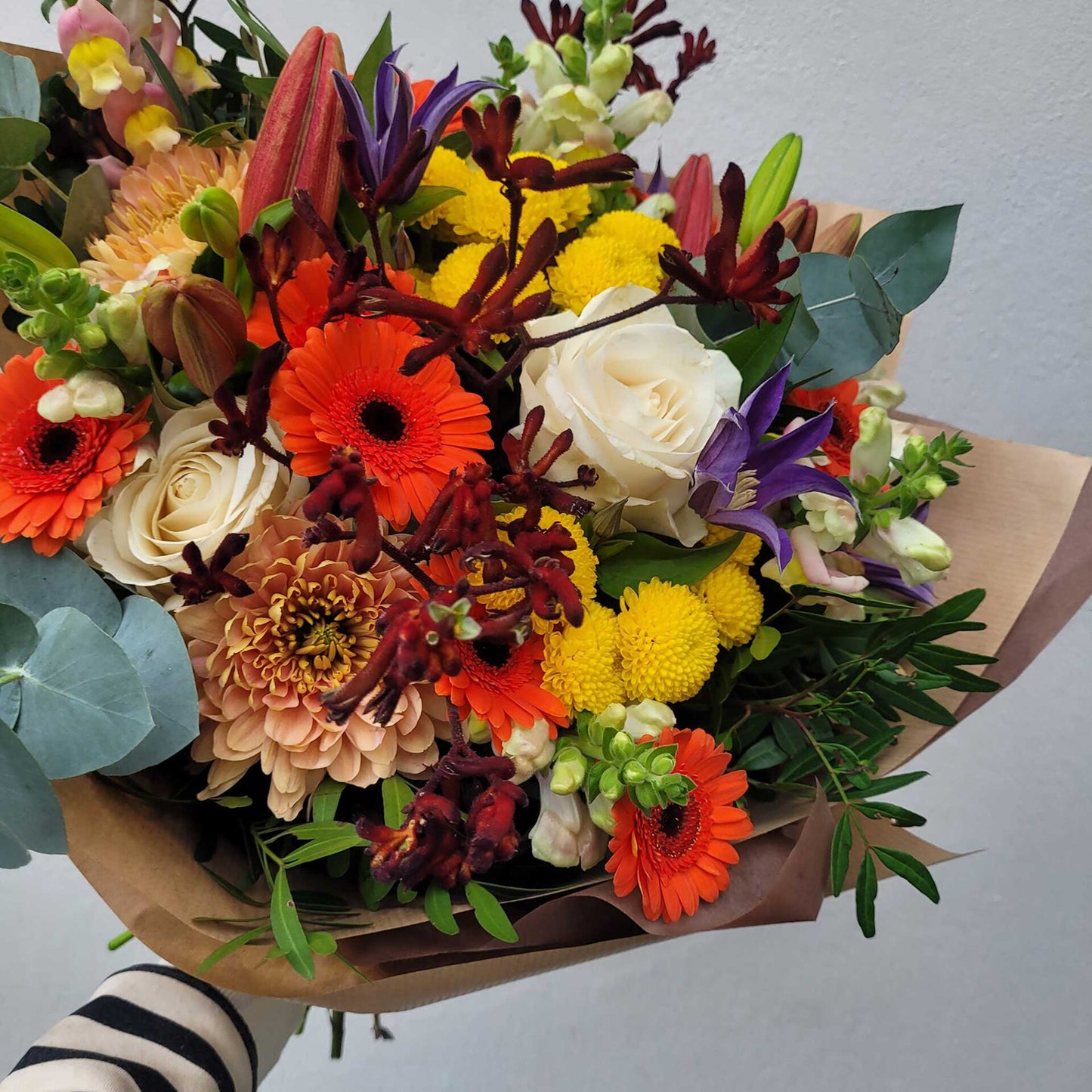 A vibrant bouquet by ReCreation Flowers' Flower Subscriptions features handmade orange gerberas, white roses, yellow button poms, lilies, chrysanthemums, snapdragons, eucalyptus leaves, and greenery set against a light background.