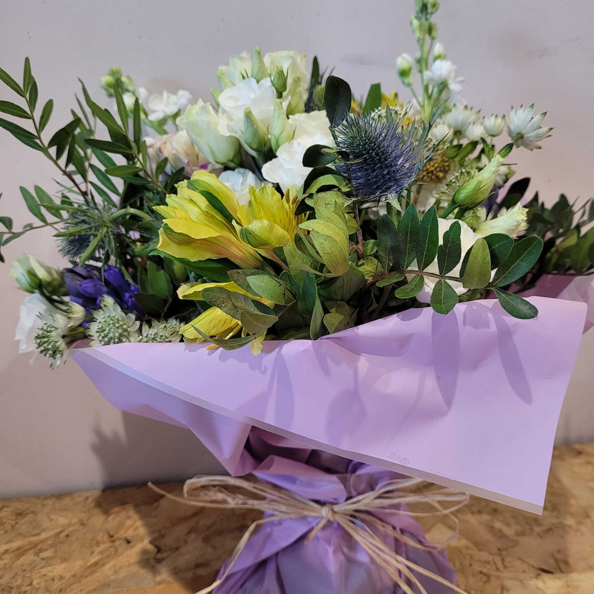 Florist Choice - Pastel by ReCreation Flowers features seasonal yellow, white, and purple blooms with green foliage, wrapped in light purple paper and twine—ideal for same-day flower delivery from your Leigh on Sea florist.