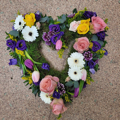 The Open Heart Funeral Flowers - Loose Style by ReCreation Flowers features pink and yellow roses, purple lisianthus, white gerberas, and green foliage—a beautiful heart-shaped tribute for funerals.